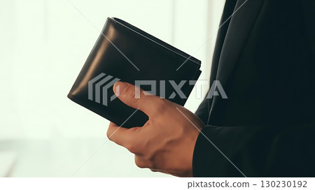 A person in a black suit holding a black wallet in their right hand close up 130230192
