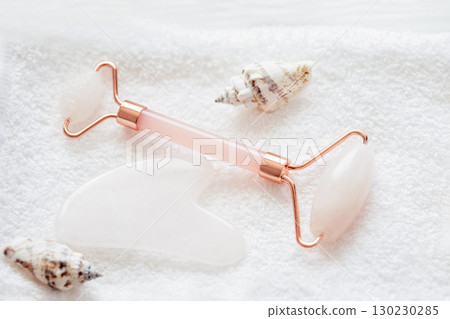 Rose quartz facial roller and gua sha stone arranged on a soft white towel with decorative seashells for a skincare and beauty spa concept Rose quartz facial roller and gua sha stone arranged on a soft white towel with decorative seashells for a skincare and beauty spa concept 130230285