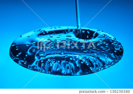 The viscous gel serum for the face flows and collects into a drop on a blue background.. The viscous gel serum for the face flows and collects into a drop on a blue background.. 130230380