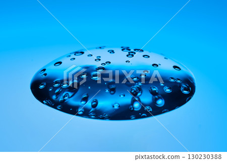 The viscous gel serum for the face flows and collects into a drop on a blue background.. 130230388