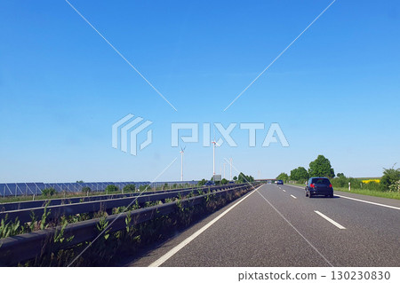 Cars drive on the highway with much windmills. Nature background with green field, trees and blue sky. Wind turbines for alternative green energy in Europe. Cars drive on the highway with much windmills. Nature background with green field, trees and blue sky. Wind turbines for alternative green energy in Europe. 130230830
