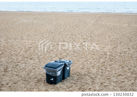 Black plastic waste containers buried in yellow sand on the beach. Black plastic waste containers buried in yellow sand on the beach. 130230832