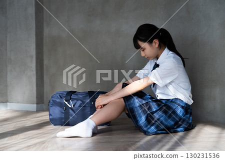 一名女學生低著頭坐在地板上的側面視圖 130231536
