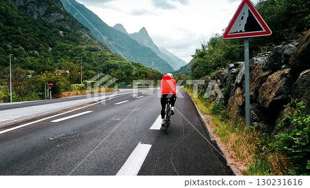 Cyclist riding on a mountain road with dramatic peaks of Belledonne in the background. Following camera view in the French Alps 130231616
