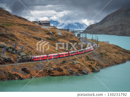 Aerial view of red train near alpine mountain lake and cloudy sky 130231792
