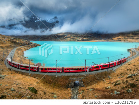 Aerial view of red train near alpine mountain lake and cloudy sky 130231799