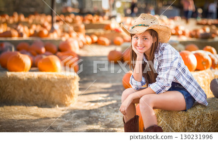 Pretty Girl Wearing Cowboy Hat Enjoying The Pumpkin Patch on a Sunny Fall Day. 130231996