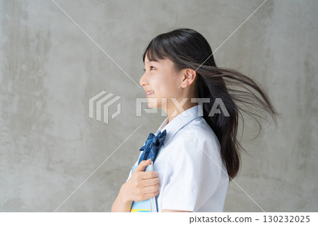 Profile of a female student with her hair blowing in the wind and holding study materials 130232025