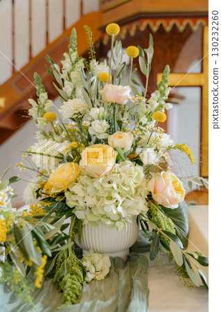 Elegant floral arrangement featuring yellow and white roses with greenery in a white vase. Perfect for weddings, events, and home decor, adding a touch of natural beauty and sophistication Elegant floral arrangement featuring yellow and white roses with greenery in a white vase. Perfect for weddings, events, and home decor, adding a touch of natural beauty and sophistication 130232260