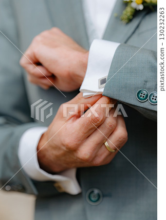 Hands adjusting cufflinks on a suit jacket, emphasizing attention to detail and preparation for a formal occasion. A subtle display of elegance with focus on attire. Hands adjusting cufflinks on a suit jacket, emphasizing attention to detail and preparation for a formal occasion. A subtle display of elegance with focus on attire. 130232263
