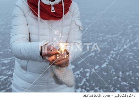 sparkler held by woman in winter landscape during foggy evening celebration. closeup. 130232275