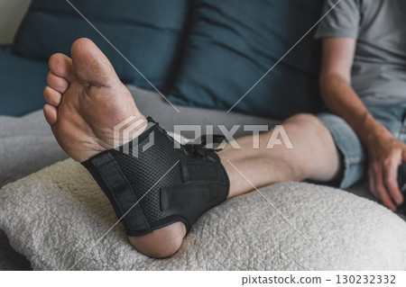 man resting on sofa with an ankle brace after sustaining an injury on leg supportive device. closeup man resting on sofa with an ankle brace after sustaining an injury on leg supportive device. closeup 130232332