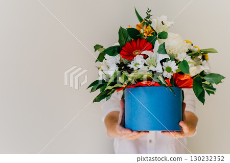 person holding large bouquet colorful flowers in blue gift box against light backdrop. closeup. 130232352