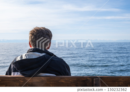 unrecognizable man enjoys serene ocean view from wooden bench on sunny day near coast. closeup. unrecognizable man enjoys serene ocean view from wooden bench on sunny day near coast. closeup. 130232362