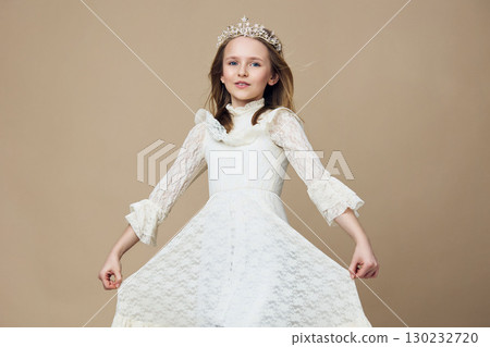 Elegant young girl in a white lace dress with a crown, showcasing confidence and joy against a neutral background, perfect for children s fashion and beauty themes 130232720