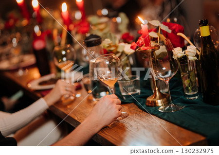 Elegant hand holding wine glass at cozy candlelit dinner with floral decor 130232975