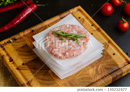Raw burger patties stacked with parchment and rosemary on a wooden board, ready to cook 130232977