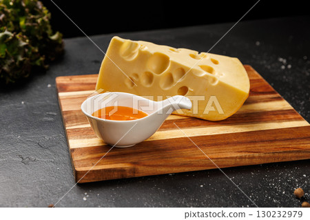 Slice of classic Swiss cheese with holes on cutting board, served with honey and berries 130232979