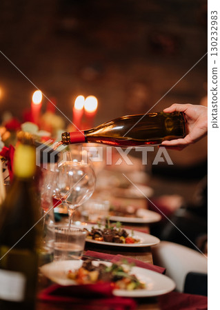 Pouring rose wine into glass at festive dinner with flowers and candlelight ambiance 130232983