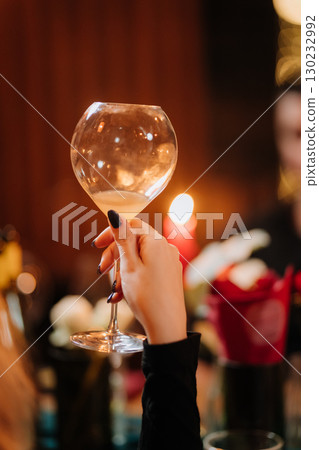 Elegant hand holding wine glass at cozy candlelit dinner with floral decor Elegant hand holding wine glass at cozy candlelit dinner with floral decor 130232992