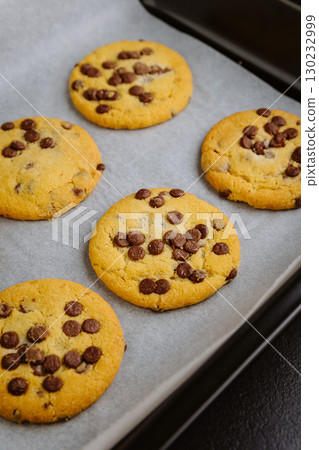 Freshly baked chocolate chip cookies in tray on parchment paper, closeup food photography 130232999