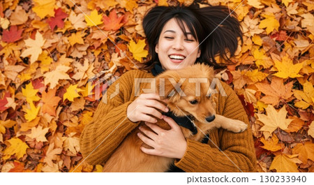 A woman playing with a dog in a park with autumn maple leaves 130233940