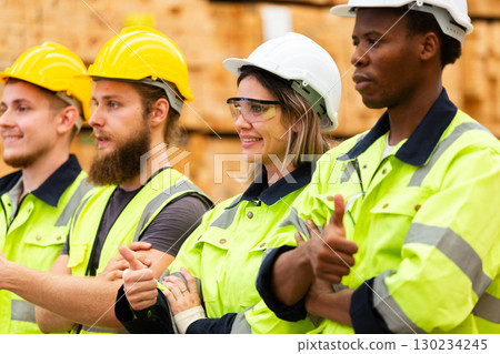 Confident warehouse workers in high visibility safety gear with crossed arms, standing in lumber storage facility, representing unity, professionalism, and industrial team motivation. Confident warehouse workers in high visibility safety gear with crossed arms, standing in lumber storage facility, representing unity, professionalism, and industrial team motivation. 130234245