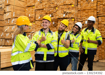 Group of multicultural industrial workers, celebrating teamwork success in a lumber warehouse while wearing safety gear and giving thumbs up. Group of multicultural industrial workers, celebrating teamwork success in a lumber warehouse while wearing safety gear and giving thumbs up. 130234392