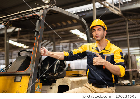 Confident industrial engineer wearing safety helmet giving a thumbs up while holding forklift in factory, representing workplace safety, approval, confidence, and job satisfaction. Confident industrial engineer wearing safety helmet giving a thumbs up while holding forklift in factory, representing workplace safety, approval, confidence, and job satisfaction. 130234503