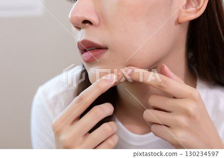Asian woman checking acne on her face in mirror and squeezing pimple, showing skincare concern, beauty problem, and facial treatment routine for clear healthy skin. Asian woman checking acne on her face in mirror and squeezing pimple, showing skincare concern, beauty problem, and facial treatment routine for clear healthy skin. 130234597
