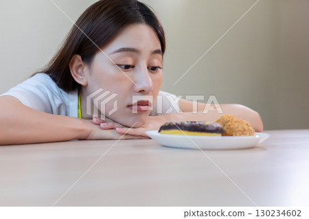 Asian woman staring at fried chicken and a donut with hesitation, representing diet struggle, food temptation, and healthy eating challenge. Ideal for concepts of nutrition decisions and weight Asian woman staring at fried chicken and a donut with hesitation, representing diet struggle, food temptation, and healthy eating challenge. Ideal for concepts of nutrition decisions and weight 130234602