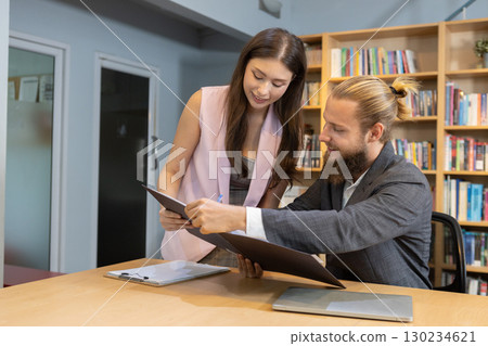 Two business professionals collaborating in modern office library, discussing documents together with teamwork and strategy for project planning and corporate success. Two business professionals collaborating in modern office library, discussing documents together with teamwork and strategy for project planning and corporate success. 130234621