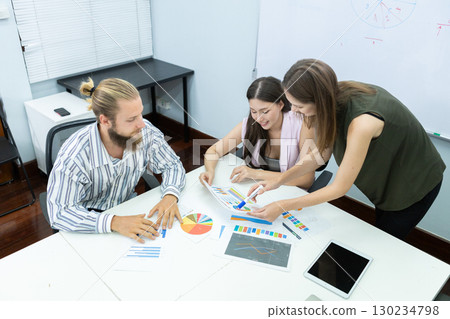 Diverse business team in meeting room discussing project strategy with charts and tablet, showing teamwork, planning, and collaboration in a modern corporate environment. 130234798
