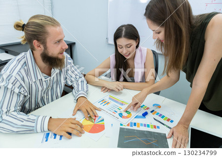 Diverse business team in meeting room discussing project strategy with charts and tablet, showing teamwork, planning, and collaboration in a modern corporate environment. 130234799
