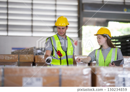 Warehouse workers in safety vests and helmets inspecting inventory and using digital tablets for stock management. Teamwork in modern logistics and industrial operations. Warehouse workers in safety vests and helmets inspecting inventory and using digital tablets for stock management. Teamwork in modern logistics and industrial operations. 130234859