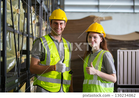 Smiling warehouse workers wearing safety gear giving thumbs up, showing teamwork, confidence, and job satisfaction in an industrial environment. Ideal for logistics and labor concepts. 130234862