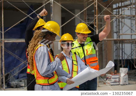Diverse team of construction workers wearing safety helmets and reflective vests looking blueprint discussing building plans on construction site for teamwork and project planning concepts. Diverse team of construction workers wearing safety helmets and reflective vests looking blueprint discussing building plans on construction site for teamwork and project planning concepts. 130235067