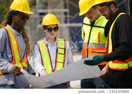 Diverse team of construction workers wearing safety helmets and reflective vests looking blueprint discussing building plans on construction site for teamwork and project planning concepts. Diverse team of construction workers wearing safety helmets and reflective vests looking blueprint discussing building plans on construction site for teamwork and project planning concepts. 130235068