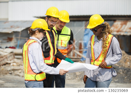 Diverse team of construction workers wearing safety helmets and reflective vests looking blueprint discussing building plans on construction site for teamwork and project planning concepts. Diverse team of construction workers wearing safety helmets and reflective vests looking blueprint discussing building plans on construction site for teamwork and project planning concepts. 130235069