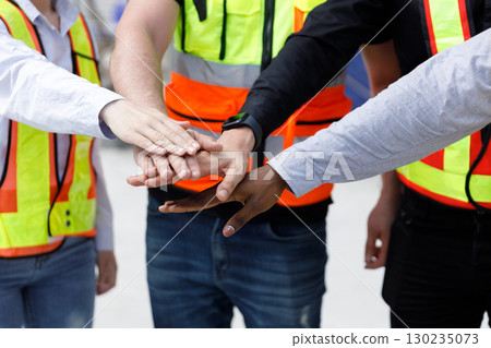 Close-up of diverse construction workers stacking hands together, wearing safety vests, symbolizing unity, teamwork, and collaboration for a successful building project and workplace harmony. 130235073