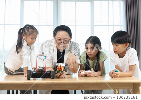 Teacher guiding diverse children in STEM robotics class, encouraging teamwork and creativity while building and programming toy robots in an education, inspiring classroom environment. 130235161