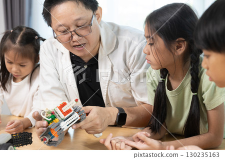 Teacher guiding diverse children in STEM robotics class, encouraging teamwork and creativity while building and programming toy robots in an education, inspiring classroom environment. Teacher guiding diverse children in STEM robotics class, encouraging teamwork and creativity while building and programming toy robots in an education, inspiring classroom environment. 130235163