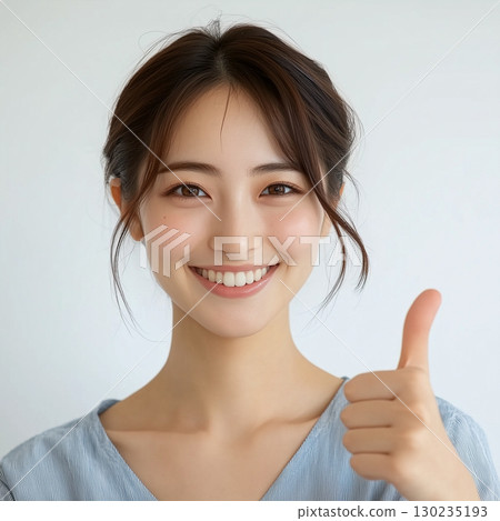 A young woman giving a thumbs up and smiling, making a "like" pose 130235193