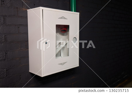 A White Emergency Fire Equipment Cabinet mounted on a Black Wall within a facility setting 130235715
