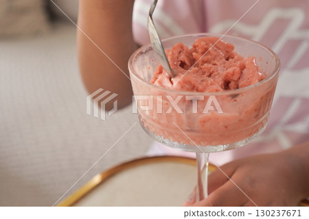 A child savors a bowl of pink ice cream in a comfortable home environment A child savors a bowl of pink ice cream in a comfortable home environment 130237671