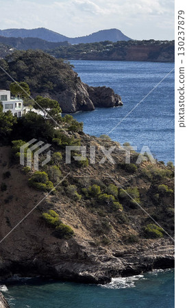 Coastal hillside of Ibiza with scattered white houses overlooking deep blue sea. Coastal hillside of Ibiza with scattered white houses overlooking deep blue sea. 130237879