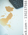Coffee spill on a white surface near a calculator 130237988
