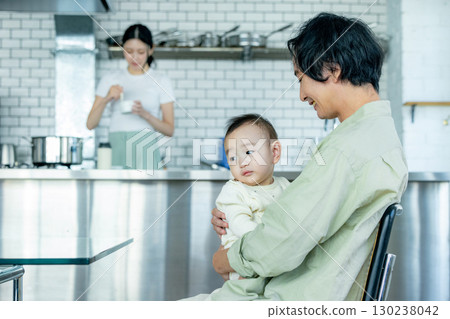 Mom cooking in the kitchen and dad taking care of the kids 130238042