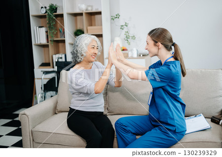 Young nurse helping elderly woman walk in the room, holding his hand, supporting. Treatment and rehabilitation after injury Young nurse helping elderly woman walk in the room, holding his hand, supporting. Treatment and rehabilitation after injury 130239329