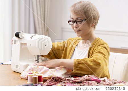 一位老年婦女高興地用縫紉機縫製衣服和配件 一位老年婦女高興地用縫紉機縫製衣服和配件 130239840